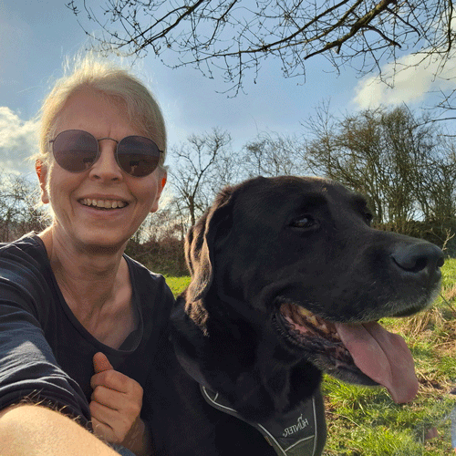 Ich, lachend in der Frühlingssonne mit meinem Labrador Retriever, im Hintergrund blauer Himmel und Äste