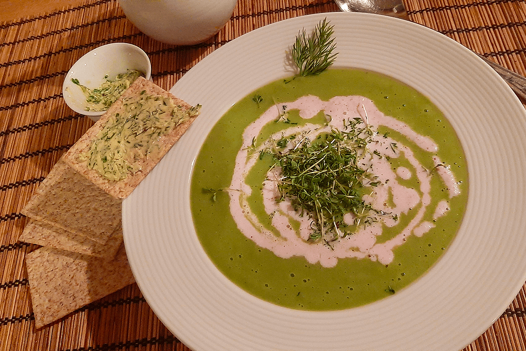 Frühlingskräuter-Suppe im weißen Teller, mit Kresse dekoriert und Vollkorncracker und Kräuterbutter daneben liegend